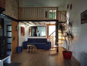 Un salon spacieux avec un canapé bleu, un plancher en bois et un escalier menant à un niveau supérieur.