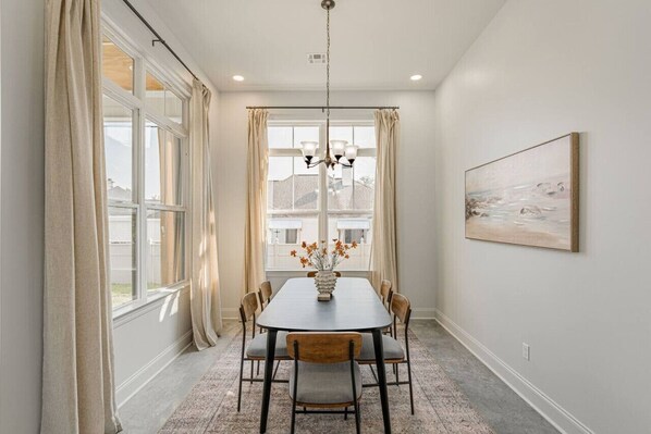 A dining area with a round table, six chairs, a vase with flowers, and a painting on the wall. - Brand New, Modern home  In The Heart Of Lafayette (Lafayette)