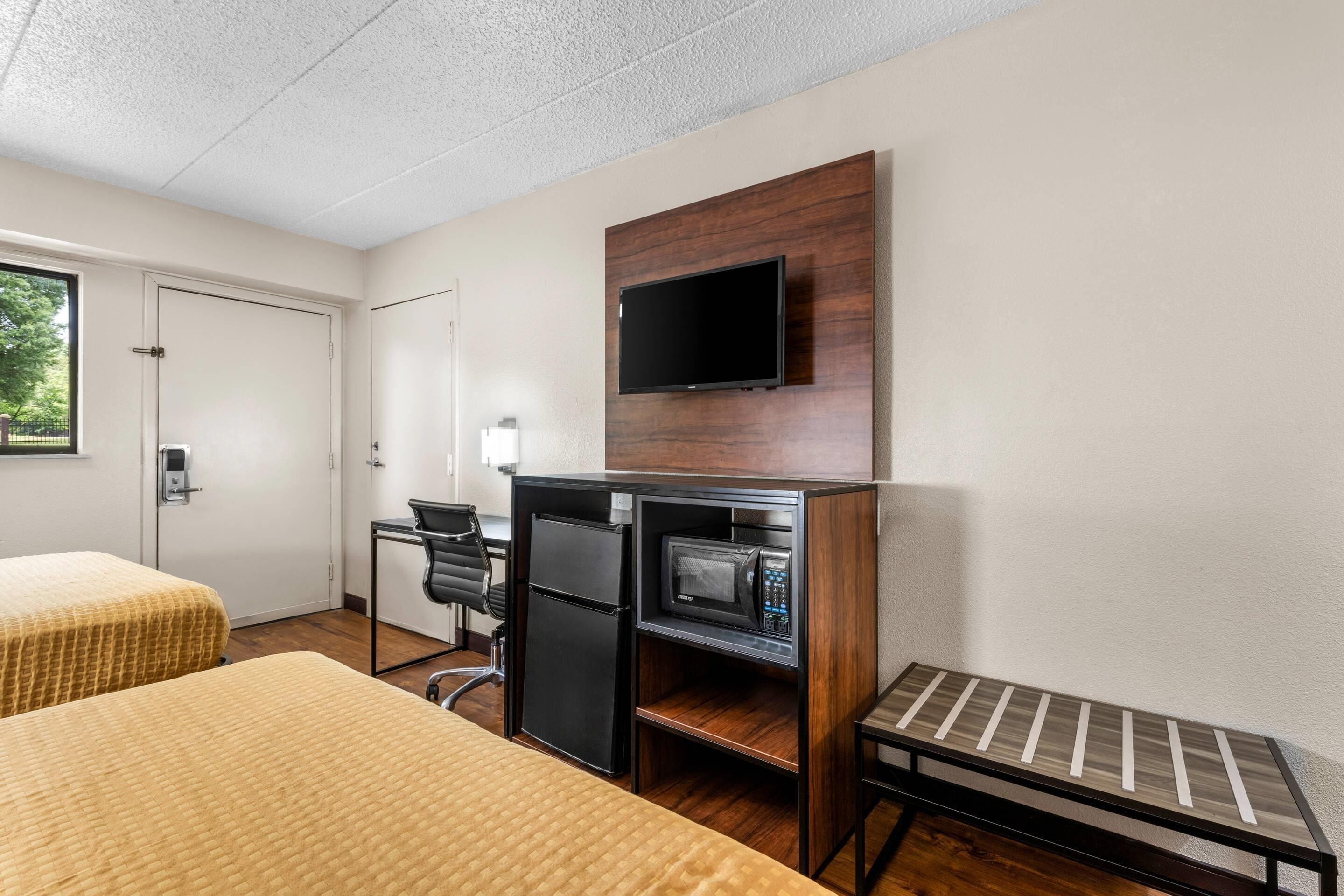 Quarto de hotel com duas camas, uma mesa com micro-ondas, frigorífico e televisão na parede, além de uma pequena mesa.