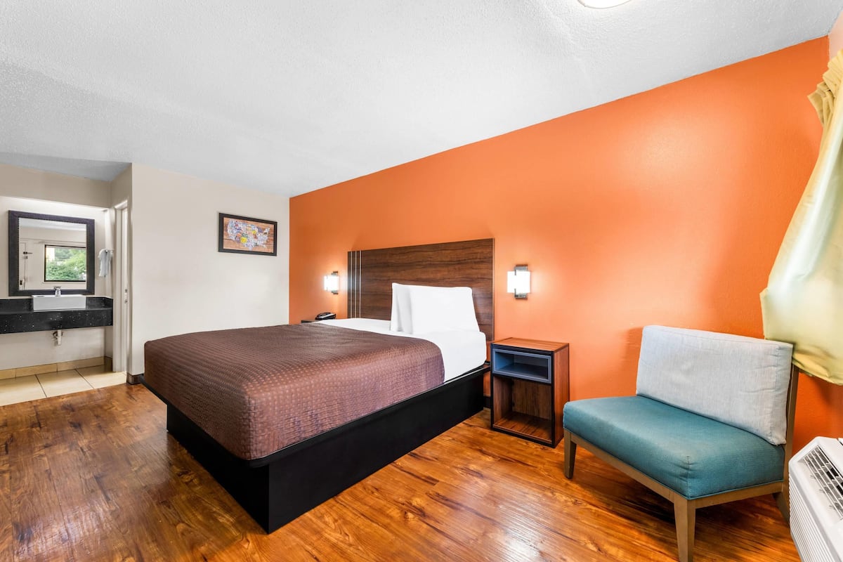 Une chambre d’hôtel avec un grand lit, une chaise, une table de chevet et un téléviseur fixé au mur.