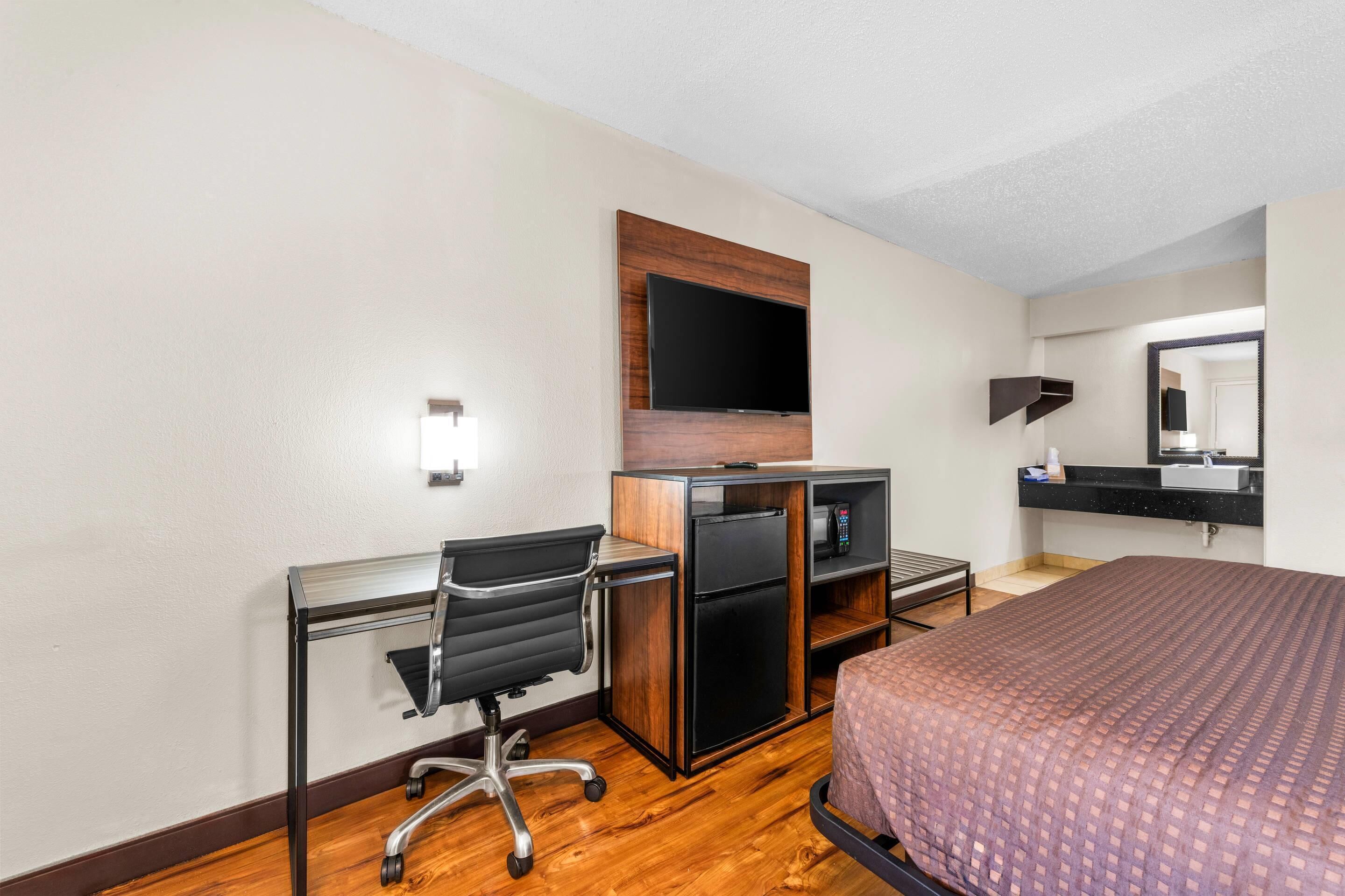 A hotel room with a desk, chair, bed, TV, and a mirror.