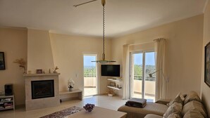 Sala de estar com lareira, sofá, televisão e varanda com cortinas.