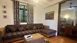 A living room with a sectional sofa, a small coffee table, and a dining area with wicker chairs and a table.