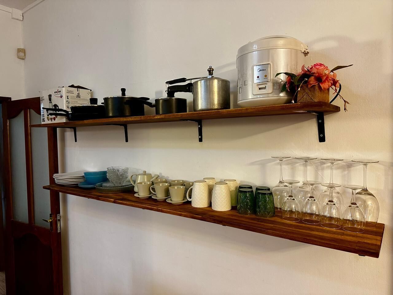 A kitchen shelf with cookware, cups, and wine glasses.