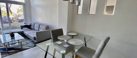 En moderne stue med et glasbord, grå sofa og abstrakt vægkunst.