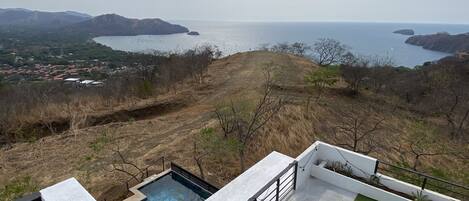 A rooftop terrace with a pool, a grassy area, and a view of a coastal landscape.