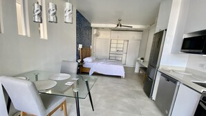 A modern hotel room with a glass dining table, a bed with white linens, a kitchenette with a microwave, and a ceiling fan. - Rooftop with ocean view, minigolf & pool and 1 queen bed (Guanacaste)