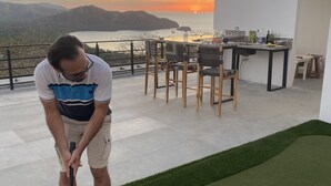 A man playing golf on a rooftop with a scenic ocean view. - Rooftop with ocean view, minigolf & pool and 1 queen bed (Guanacaste)