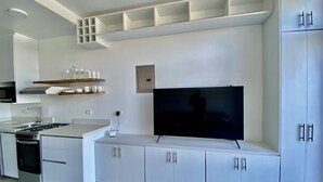 A modern kitchen with white cabinetry, a built-in stove, and a television mounted on the wall. - Rooftop with ocean view, minigolf & pool and 1 queen bed (Guanacaste)