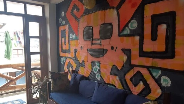 Habitación con sofá azul, un mural abstracto colorido y vistas al exterior a través de una puerta de cristal.