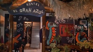 Entrada a un hostal con un letrero que dice "Hostel El Gran Azul", decorado con murales coloridos y plantas.