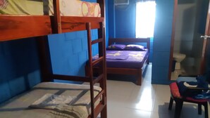 Un dormitorio con literas, una cama individual, una silla y un baño visible a través de una puerta abierta.