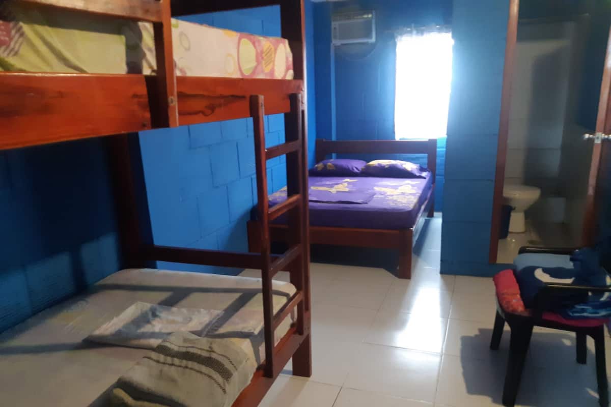 A dormitory room with bunk beds, a single bed, a chair, and a bathroom visible through an open door.