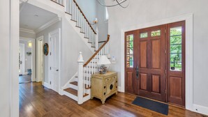 Eine Holztreppe mit weißen Geländern, eine Holztür mit Glasfeldern und ein kleines Holzschränkchen mit einer Lampe.