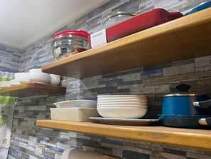A kitchen shelf with various kitchenware including bowls, plates, and a blue pot.