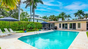 A swimming pool with lounge chairs and umbrellas, surrounded by palm trees and a house in the background. - Best Location in Olde, South Naples! (Naples)