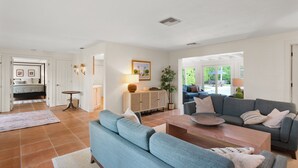 A spacious living room with a blue sofa, a wooden coffee table, and a grey couch. There is a dining area with a table and chairs, and a kitchen visible in the background. - Best Location in Olde, South Naples! (Naples)