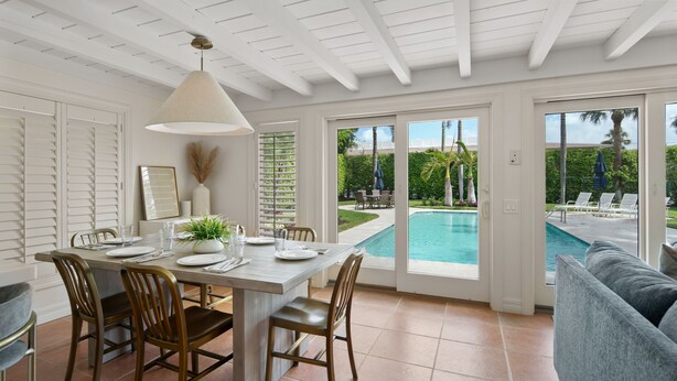 A dining area with a pool view, featuring a table set for four, chairs, and a hanging light fixture. - Best Location in Olde, South Naples! (Naples)
