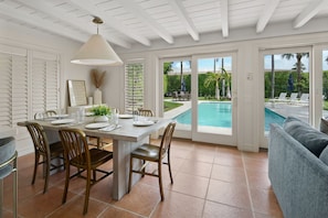 Comedor con vista a la piscina, con una mesa para cuatro, sillas y una lámpara colgante.