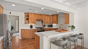 A modern kitchen with wooden cabinets, a stainless steel refrigerator, an island with bar stools, and a large oven. - Best Location in Olde, South Naples! (Naples)