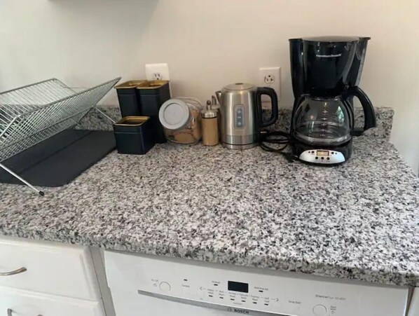 A kitchen counter with a coffee maker, kettle, and containers.
