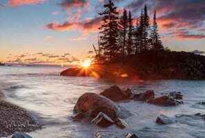 Un atardecer sobre una costa rocosa con árboles al fondo.