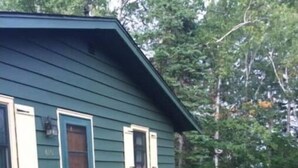 A green house with a wooden deck and a small porch. - Iconic Knotty Pine Cabin in Charming Grand Marais (Grand Marais)