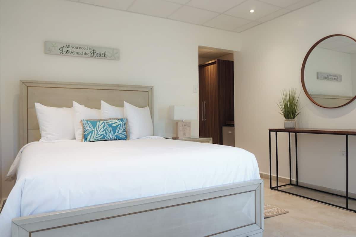 A bedroom with a large bed, a bedside table with a lamp, a small potted plant, and a mirror on the wall.