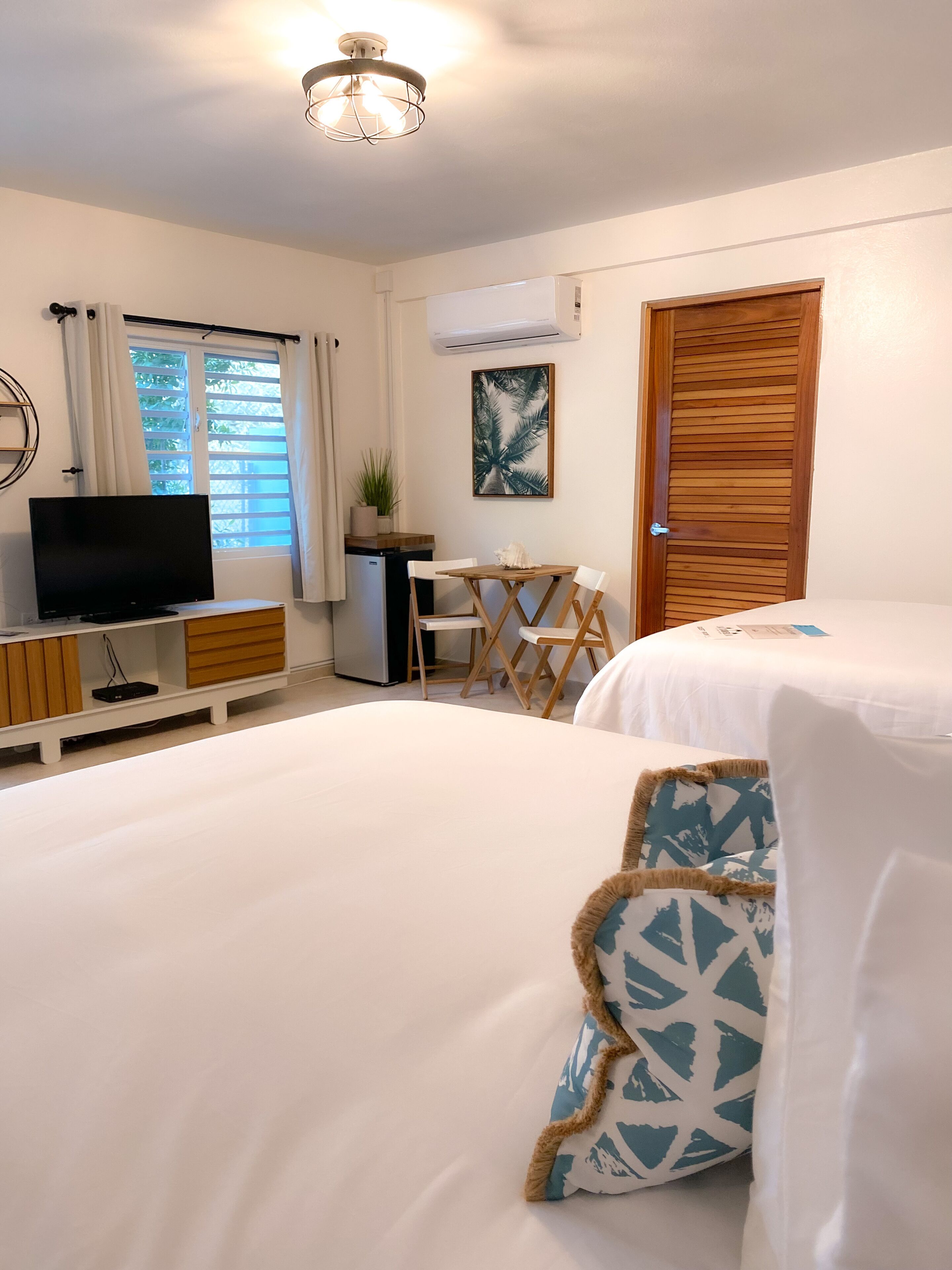 A hotel room with a bed, a TV, a desk, and a window with curtains.