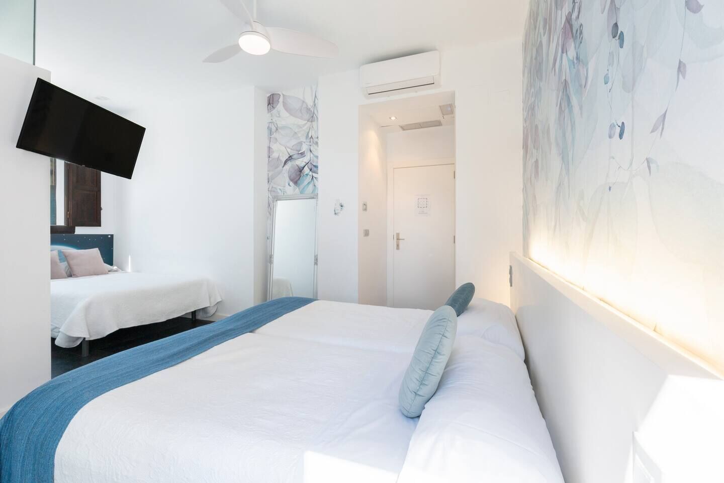 Habitación de hotel con una cama grande, otra más pequeña, un televisor de pantalla plana, un equipo de aire acondicionado y una puerta que da a otra habitación.