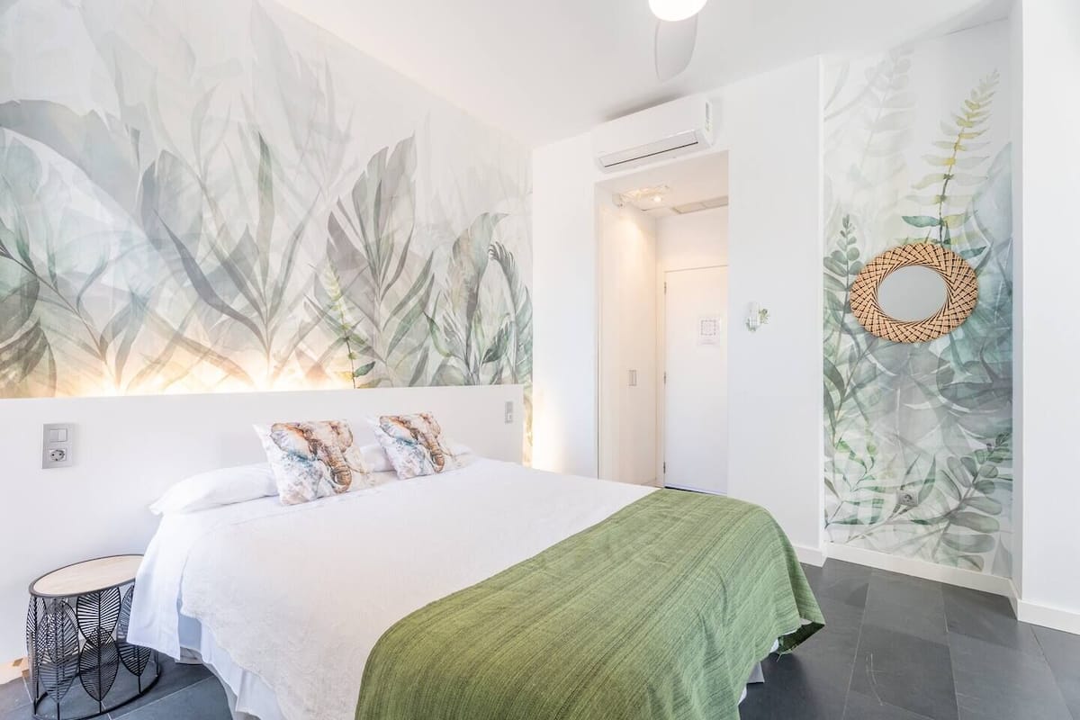 A modern bedroom with a large bed, a green throw blanket, and leaf-patterned wall art.