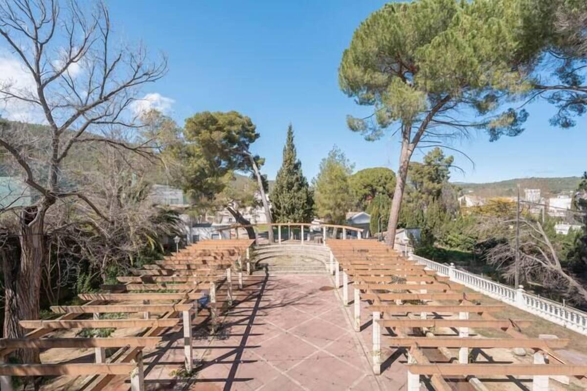 A long, empty pathway with wooden benches and a stone bridge in the distance.