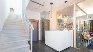 Un espace d’accueil moderne avec un comptoir de réception blanc, un mur en verre et un escalier doté de rampes bleues.