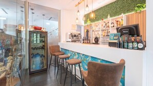 Un espace bar moderne comprenant un comptoir, des tabourets, une machine à café et une variété de bouteilles et de verres.