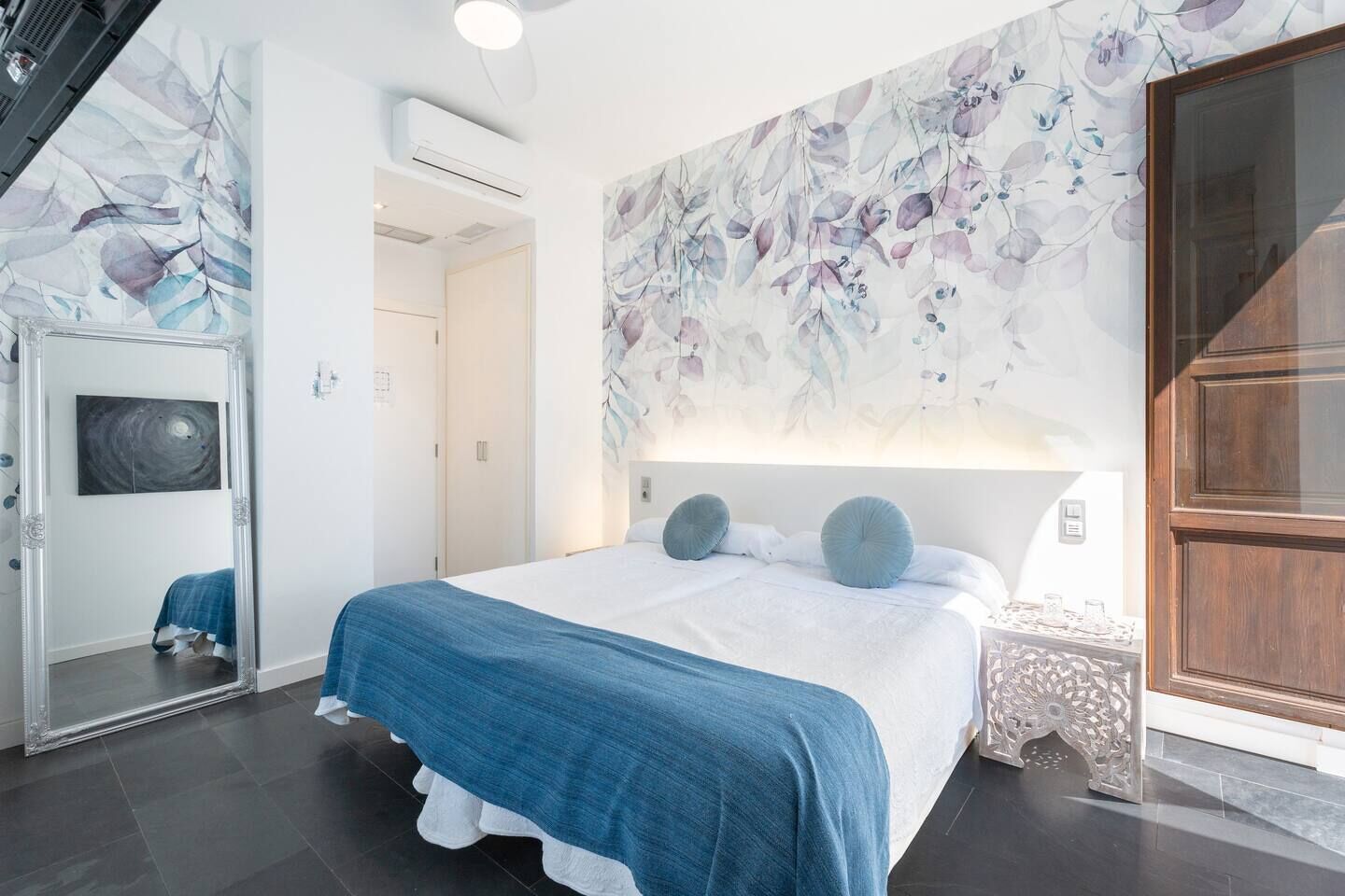 Un dormitorio moderno con una cama grande, un mural floral, un espejo y un armario de madera.