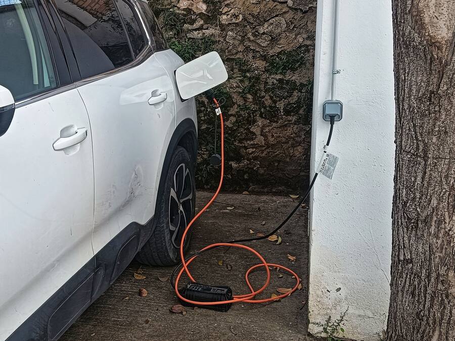 Une voiture blanche est garée à côté d’un arbre et est branchée à une prise électrique.