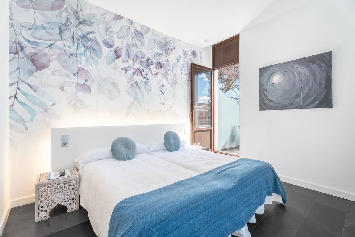 A modern bedroom with a large bed, a blue blanket, and a floral wall mural.