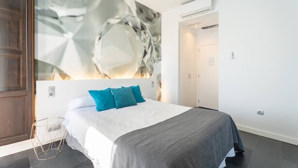 Une chambre moderne avec un grand lit, une œuvre d’art murale aux motifs géométriques et une porte en bois.