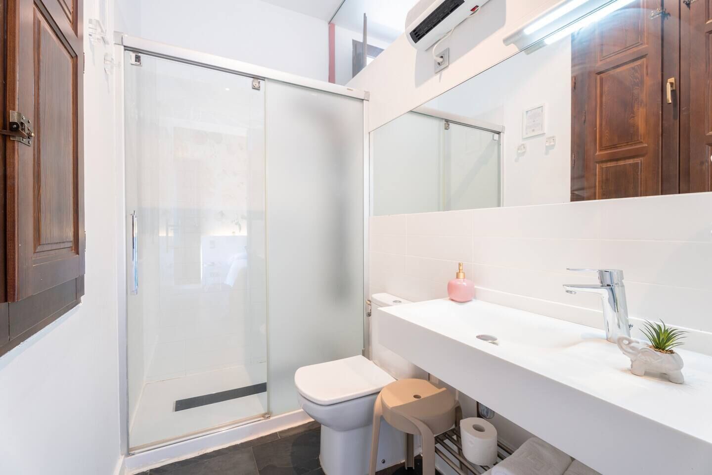 A modern bathroom with a glass shower enclosure, a white sink with a mirror above, and a toilet.