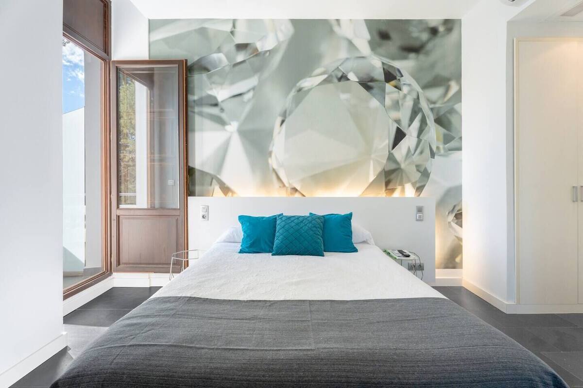A modern hotel room with a large bed, a view of the outdoors, and a unique wall art piece.