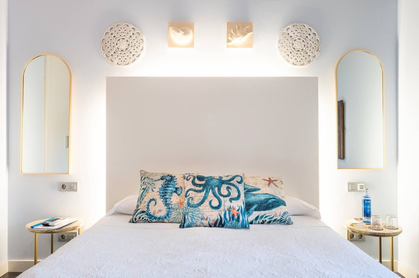 Una camera da letto con un letto grande, due comodini, uno specchio fissato alla parete e applique decorative.