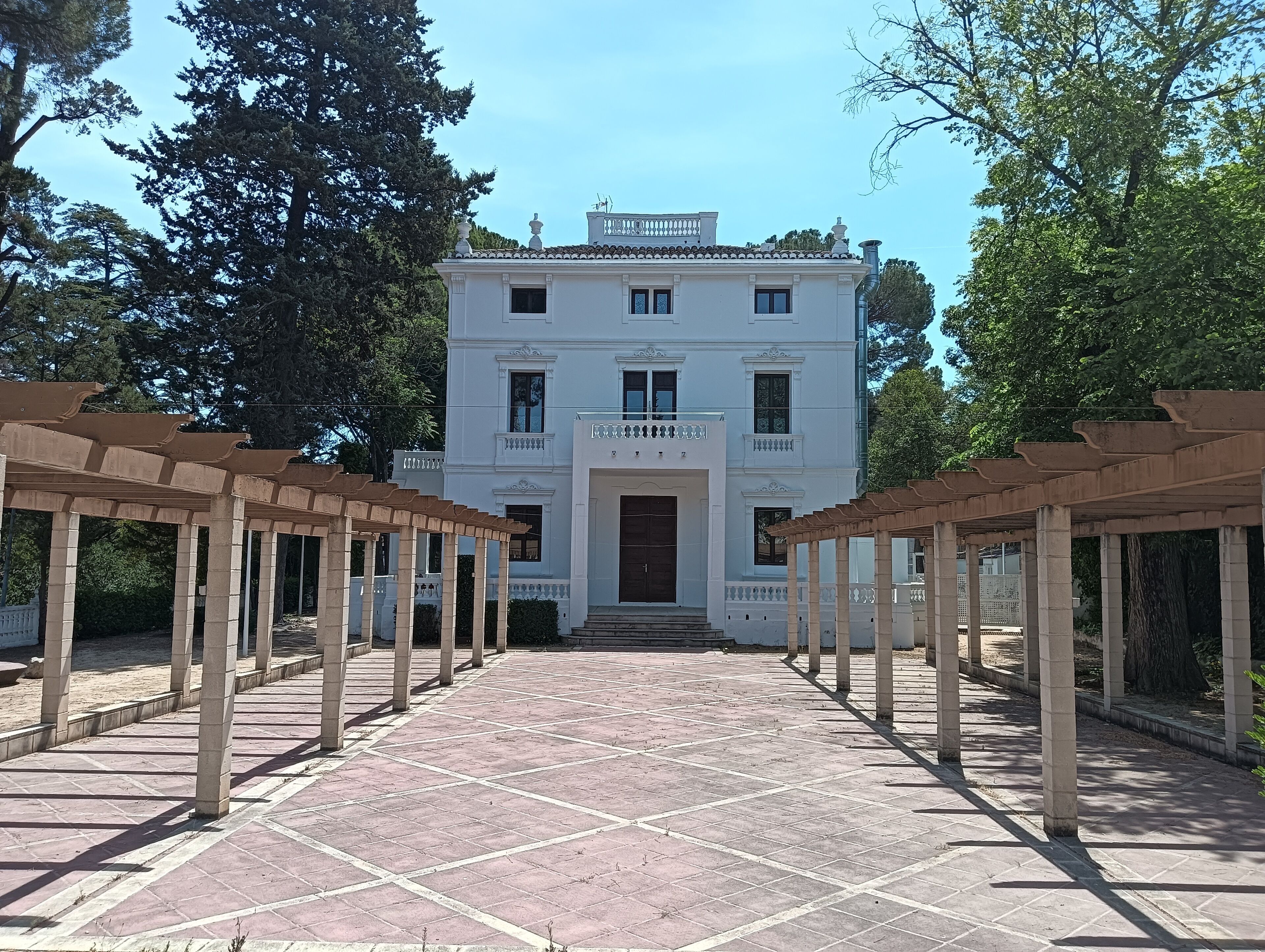 Un edificio blanco con fachada simétrica, una entrada central y un camino pavimentado que lo conduce.