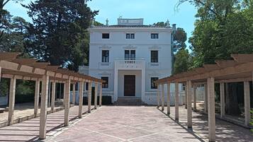 Un edificio blanco con fachada simétrica, una entrada central y un camino pavimentado que lo conduce.