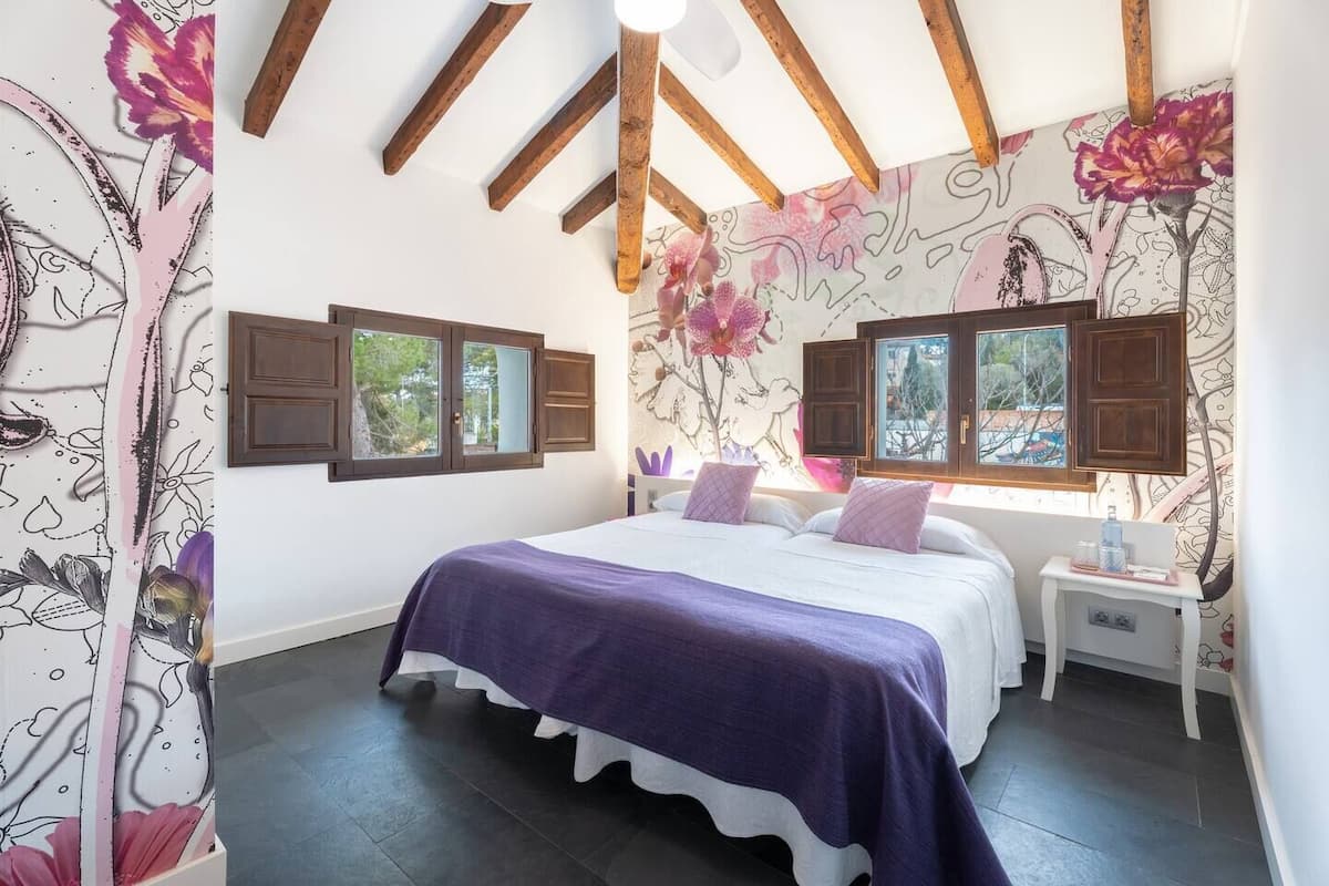 A bedroom with a large bed, wooden beams, and floral wallpaper.