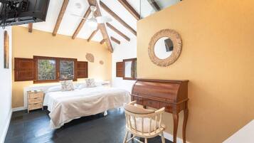 A bedroom with a bed, a wooden dresser, a chair, a mirror, and a television mounted on the ceiling.