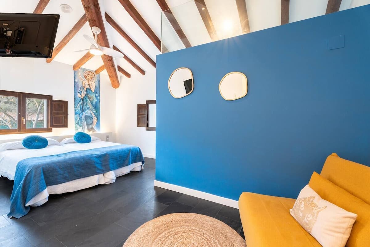 A bedroom with two beds, a blue wall, and a yellow sofa.