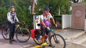 Dos ciclistas con bicicletas estacionadas cerca de un edificio con un letrero que dice '1893 HOTEL BOUTIQUE Restaurante HC'.