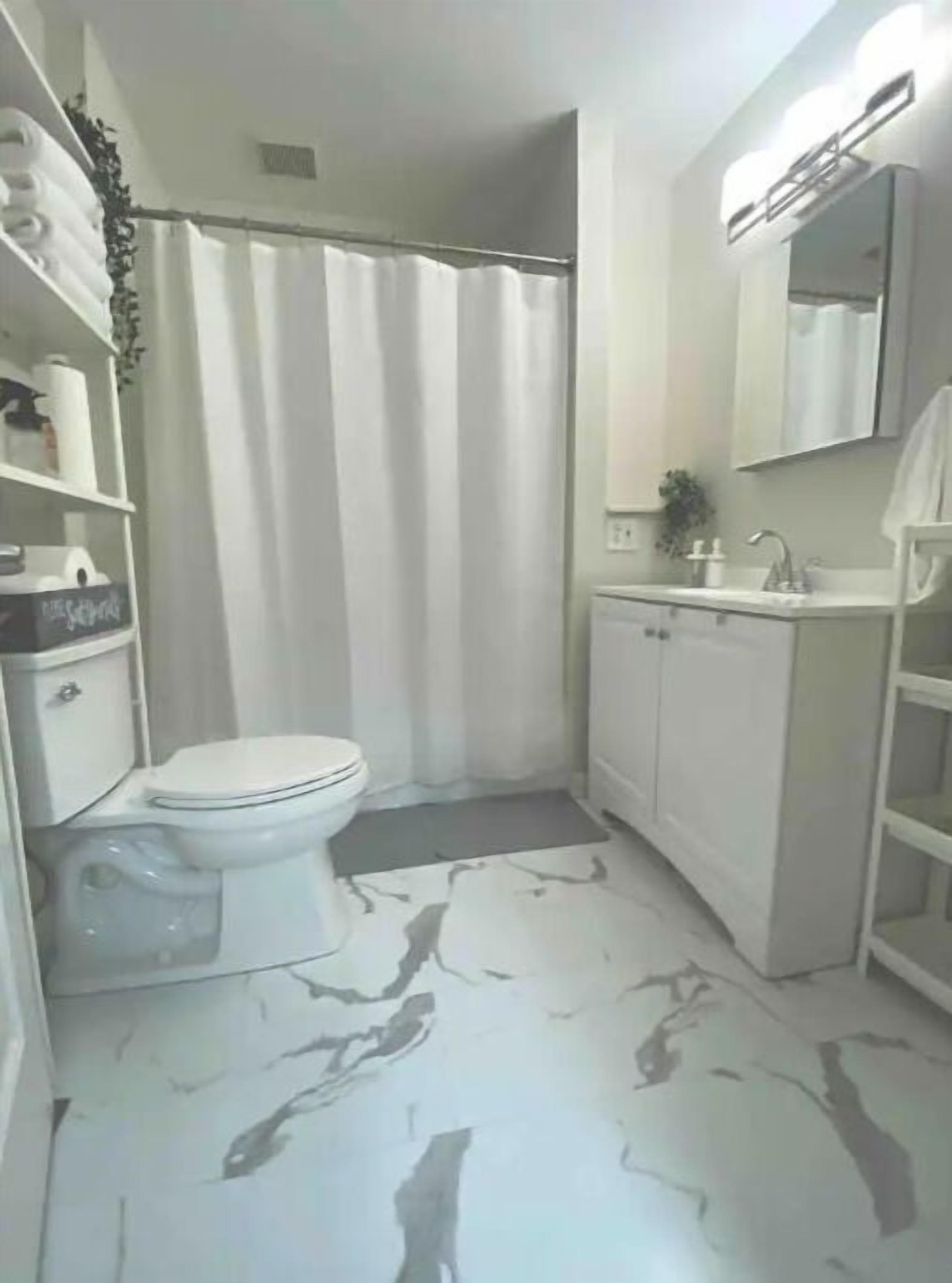 A small, compact bathroom with a toilet, a shower curtain, a sink, and a mirror.