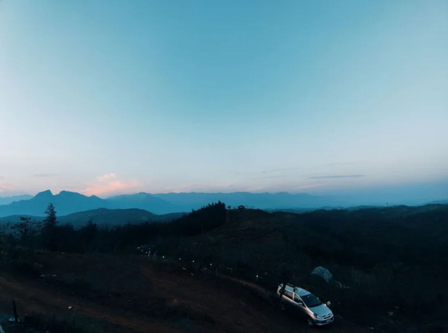 Une voiture est garée sur un chemin de terre, avec un paysage montagneux en arrière-plan.