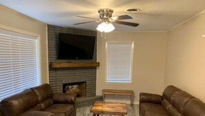 Ein Wohnzimmer mit zwei braunen Ledersofas, einem Holztisch, einem Kamin und einem Deckenventilator.
